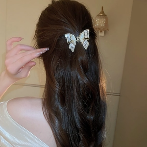 Dettaglio macro di un fermaglio per capelli a farfalla dorato con zirconi e madreperla