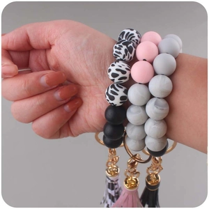 Close-up of three silicone beaded wristlet keychains with leather tassels on a model wrist