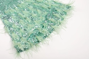 Detail of mint green sequin dress featuring soft feathers and elegant pearl embellishments