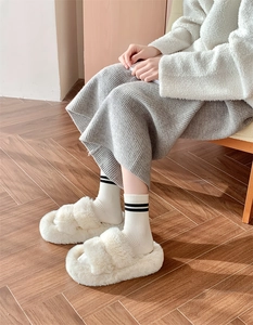 Close-up of fluffy white open-toe plush slippers worn with striped wool socks on wood floor