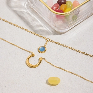 Detail of gold horseshoe necklace and blue opal pendant on sandy background