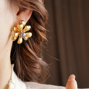 Detail of a large 18k gold plated flower earring featuring a purple pearl on a female model