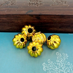 Five golden pumpkin-shaped plastic electroplated beads on a vintage fabric background
