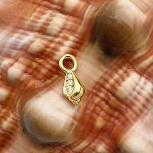 Macro shot of gold shell pendant with three zircons on a textured brown background