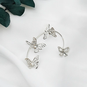 Detailed macro view of silver butterfly ear cuff with sparkling zircon inlay on white silk