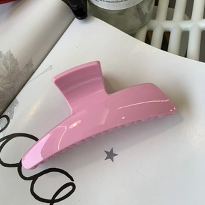 Glossy pink rectangular hair claw clip shown in a lifestyle desk setting with magazines