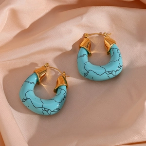 Macro shot of U-shaped gold earrings with turquoise marble texture on pink silk fabric