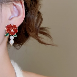 Detailed view of red rose earrings with white pearls on a model ear for visual scale