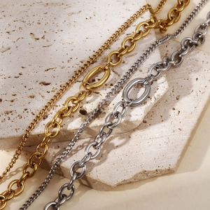 Close-up of dual-layer gold and silver stainless steel chains on a stone surface