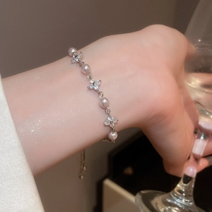 Detail of pink pearl bracelet with flower charm worn by a model in a luxury setting