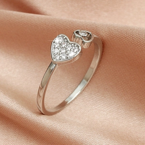 Macro detail of silver heart ring with sparkling rhinestones on pink silk background