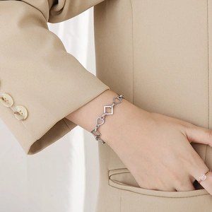 Detail of silver heart and geometric chain bracelet on model wrist with soft lighting