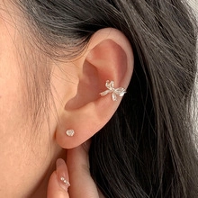 Close-up of silver bow ear cuff with pavé zircons and minimalist stud on model ear