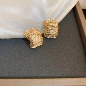 Macro shot of gold geometric C-shaped earrings with layered textured metal ripples