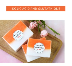 Dual-tone Kojic Acid and Glutathione soaps in 100g and 200g sizes on a wooden tray