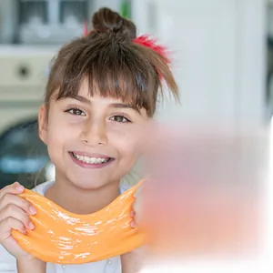 Close-up of a girl stretching orange silk slime with various colorful crystal slime kits
