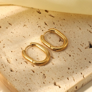 Close-up of golden U-shaped oval earrings on beige stone and soft fabric background