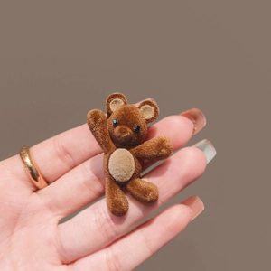 Cute brown flocked bear hair clip with blue bead eyes held in hand on neutral backdrop