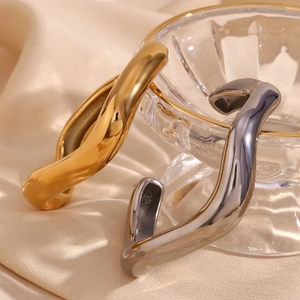 Close-up of gold and silver irregular liquid wave open bracelets on beige silk fabric