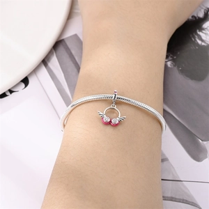 Close-up of silver snake chain bracelet with a pink enamel angel wing charm on model
