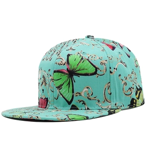 Detail of turquoise flat brim baseball cap featuring butterfly and gold filigree patterns