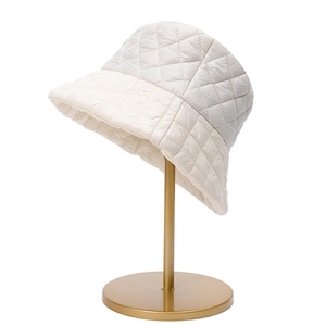 Detalle de gorro de pescador acolchado crema con textura de rombos en soporte dorado