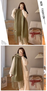 Detail showing soft sage green knitted scarf with long tassels in a cozy lifestyle setting