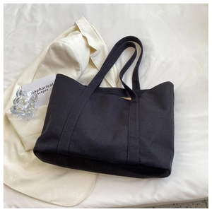 Detailed view of large black canvas tote bag on textured white fabric background