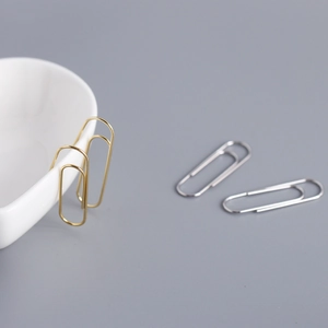 Detailed view of minimalist gold and silver paperclip earrings on a white bowl and table