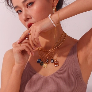Macro detail of 18K gold-plated jewelry set with pearls and enamel pendants on model