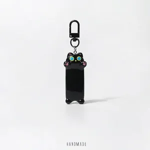 Cute black cat keychain with bright blue eyes and pink paws on white background
