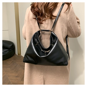 Rear view of model wearing a large black leather crossbody bag with gold metal buckles
