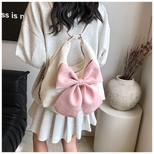 Detail shot of a cream hobo bag featuring a large pink bow and chain strap on a model