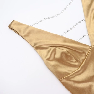 Detailed close-up of golden satin V-neck dress with sparkling rhinestone chain straps