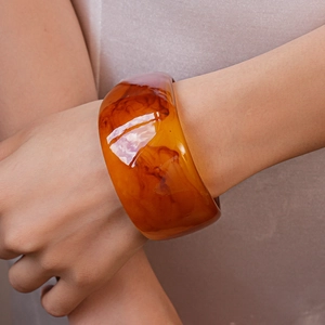 Detailed view of wide amber resin bangle featuring swirling textures on a wrist