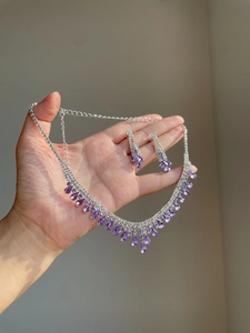 Detailed view of silver necklace and earrings set with purple teardrop crystals and rhinestones