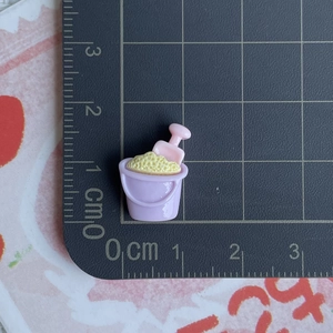Gros plan d'un seau de plage miniature violet avec pelle rose et sable jaune sur échelle