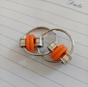 Detail of metal fidget chain toy with orange silicone rings on lined paper background