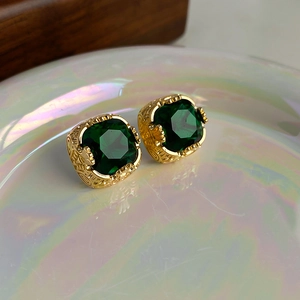Dettaglio di orecchini vintage placcati in oro con pietre smeraldo quadrate e intagli