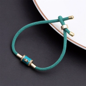 Detail of teal woven bracelet featuring evil eye enamel bead and gold adjustable clasp