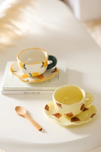 Macro detail of hand-painted ceramic coffee cups with lemon and bear patterns and wave saucers