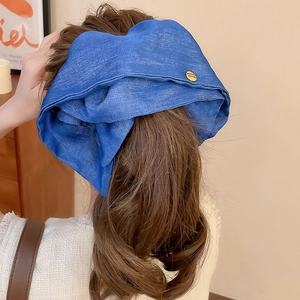 Detailed view of large blue denim fabric hair claw clip with a round gold metal emblem