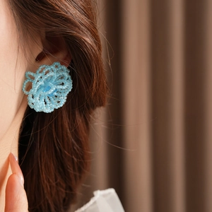 Close-up of blue woven crystal flower stud earring worn by a model in soft lighting