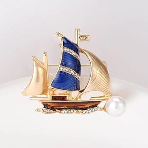 Macro shot of gold sailboat brooch with blue enamel, crystals, and a large pearl accent