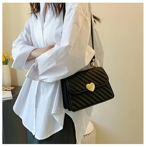 Detail of black crossbody bag with pleated stitching and heart-shaped gold metal clasp