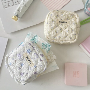 Flat lay of a floral quilted cotton sanitary pad pouch on a white desk with daily accessories