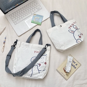 Detalle de dos bolsos de lona blancos con estampados de oso y conejo y correas grises