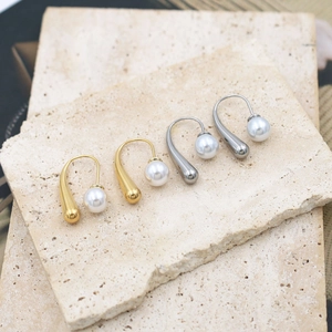 French style 18k gold and silver drop pearl earrings on textured stone surface