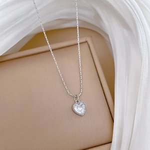 Detailed close-up of a silver heart pendant necklace with rhinestones on silk fabric