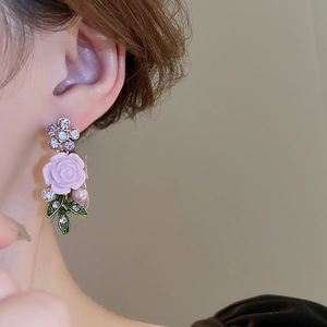 Detailed shot of flower earrings with pink rose, purple stone, leaves and pearl